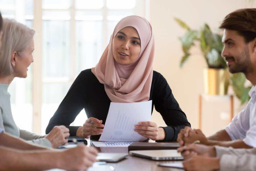 Young asian muslim businesswoman executive wear hijab discussing paperwork financial results consult clients employees group explain project plan at corporate briefing sit at company meeting table