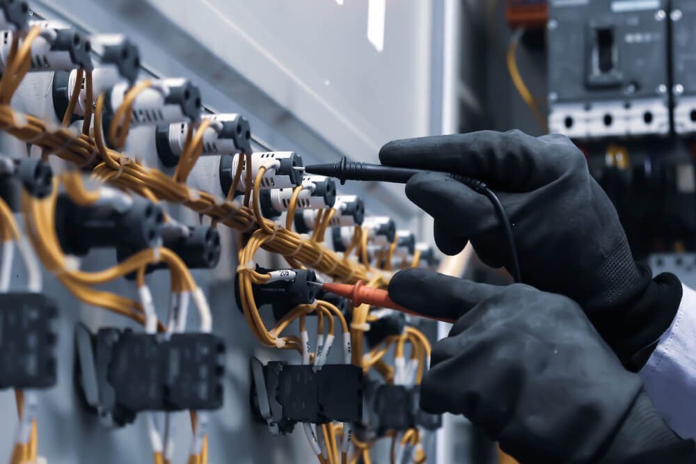 Electrical engineer using digital multi-meter measuring equipment to check voltage of electrical current at circuit breaker in main power distribution board.