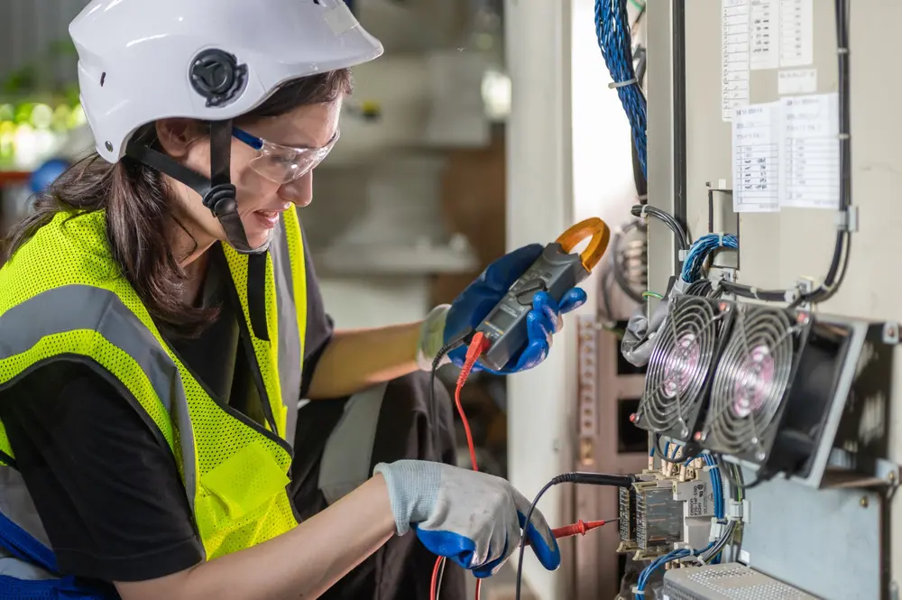 Woman Electrician engineer work check tester measuring voltage and current of power electric line in electricity cabinet control. Workers use clamp meter to measure current electrical wires