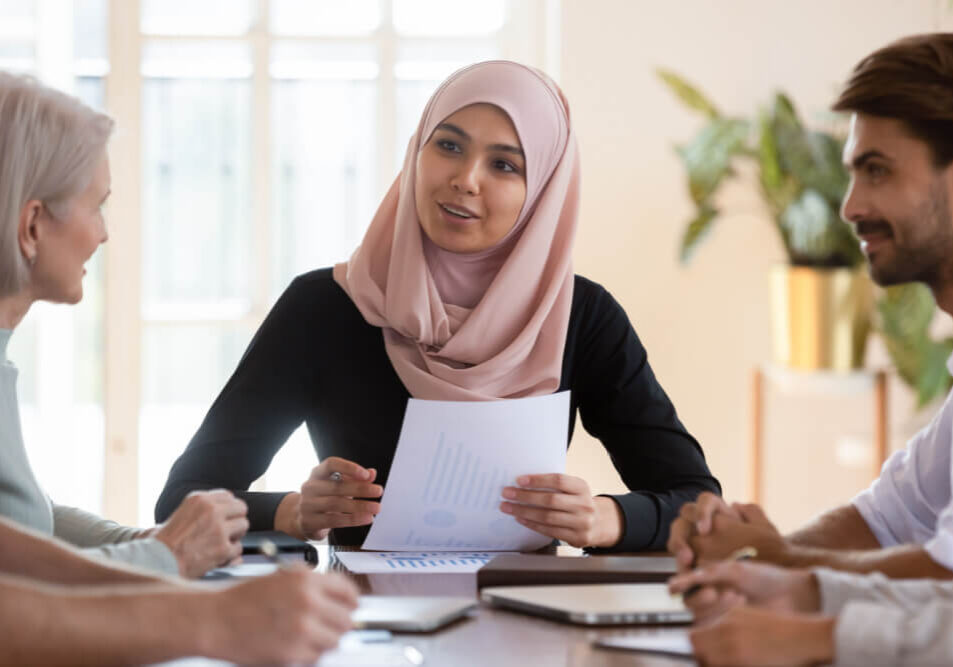 Young asian muslim businesswoman executive wear hijab discussing paperwork financial results consult clients employees group explain project plan at corporate briefing sit at company meeting table