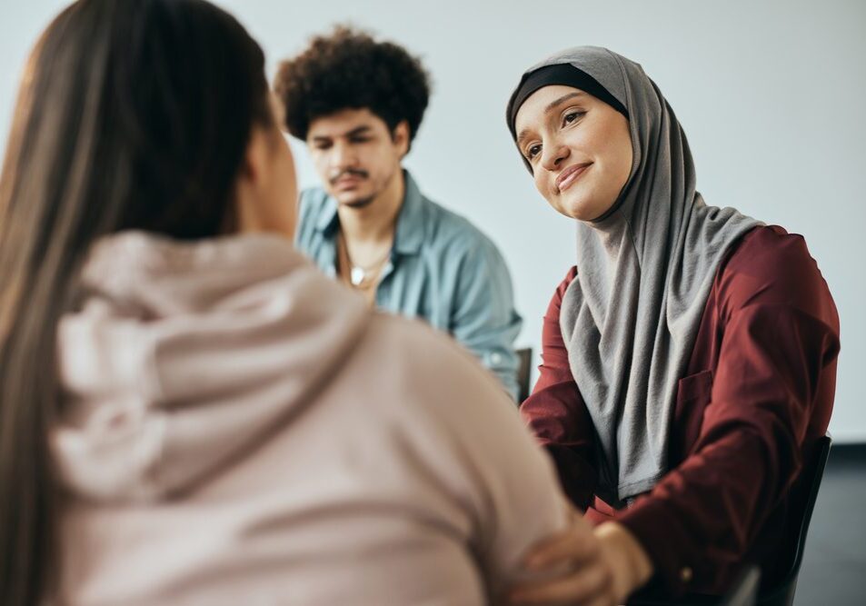 Caring Middle Eastern woman supporting new attender of group therapy to talk about herself during the meeting at mental health center.
